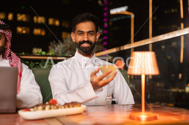 رجل سعودي بالثوب في مطعم على السطح ليلاً