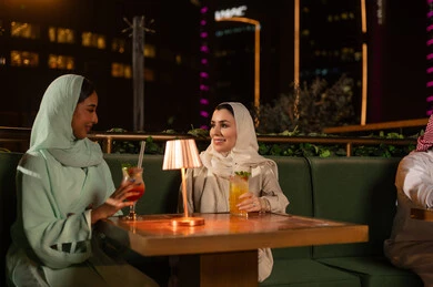 نساء سعوديات في مطعم خارجي مع أضواء المدينة ليلاً