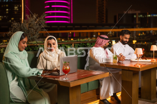 أشخاص سعوديون في مطعم على السطح وأفق المدينة ليلاً