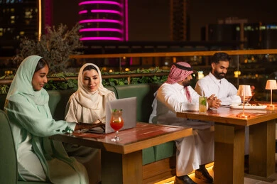 أشخاص سعوديون في مطعم على السطح وأفق المدينة ليلاً