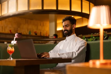 Saudi Man Using Laptop in Modern Restaurant Lounge