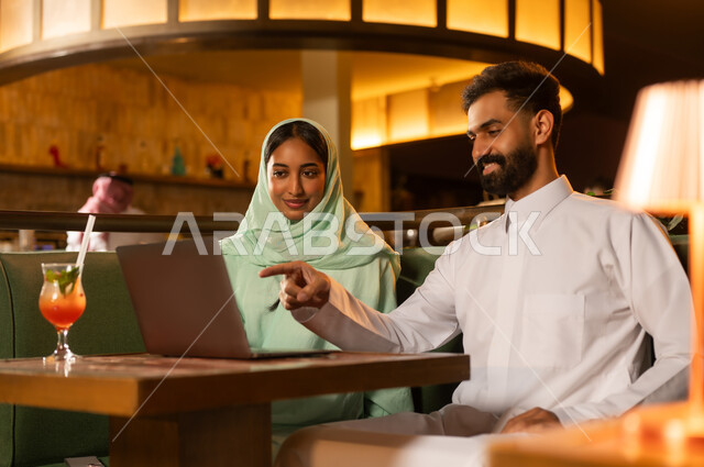رجل وامرأة سعوديان مع حاسوب محمول في مطعم
