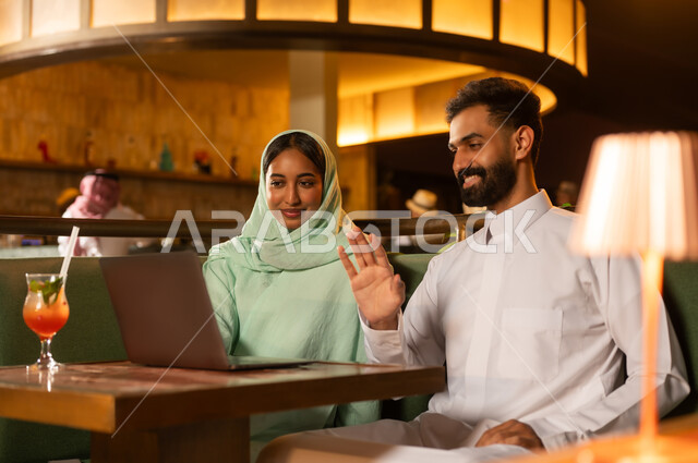 Saudi Couple Using Laptop for Video Call in Restaurant