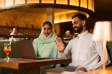 Saudi Couple Using Laptop for Video Call in Restaurant