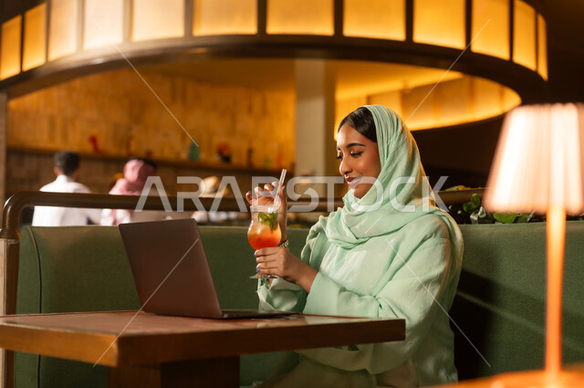 امرأة سعودية عربية تستخدم اللابتوب في مطعم داخلي بإضاءة دافئة