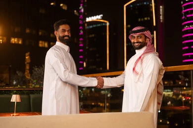 مصافحة رجال سعوديين بالزي التقليدي على شرفة مدينة ليلية