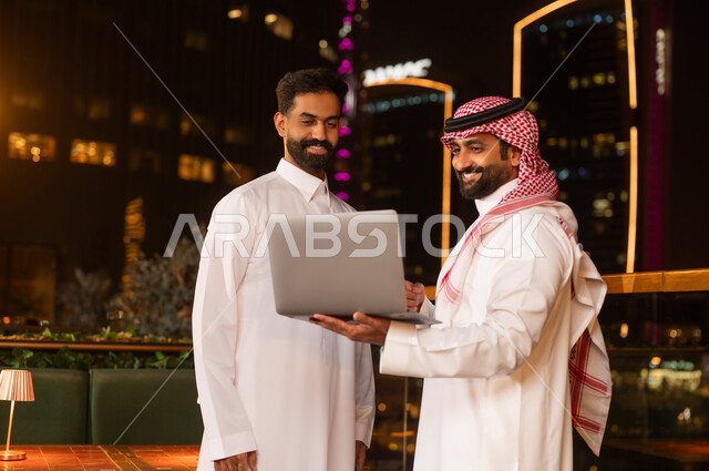 Saudi Businessmen Using Laptop on City Terrace at Night