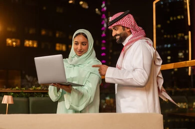 رجل وسيدة أعمال سعوديان يعملان على المحمول ليلاً