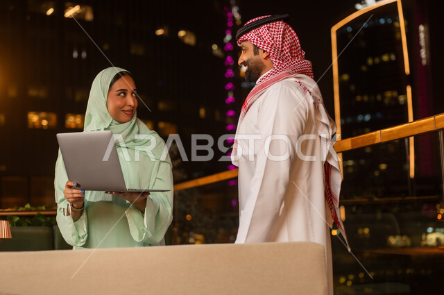 رجل وامرأة من السعودية يعملان على المحمول ليلاً