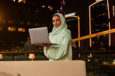 امرأة عربية تعمل على المحمول في سطح بدبي ليلا