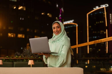 امرأة عربية مع كمبيوتر محمول في مدينة ليلاً