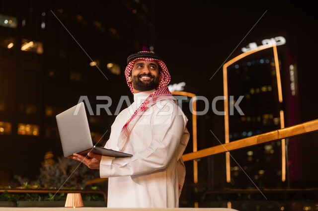 رجل أعمال سعودي يحمل كمبيوتر محمول في المدينة ليلاً