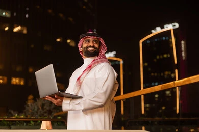رجل أعمال سعودي يحمل كمبيوتر محمول في المدينة ليلاً