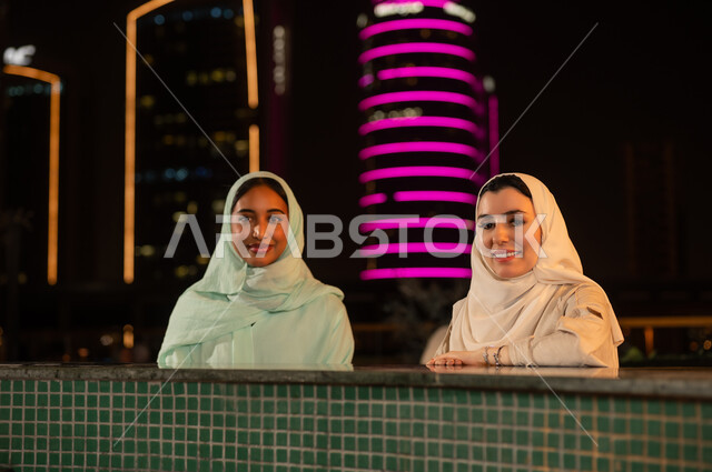 نساء سعوديات أمام ناطحات سحاب مضيئة ليلاً