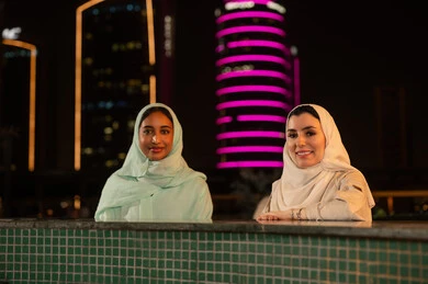 نساء سعوديات أمام ناطحات سحاب مضيئة ليلاً