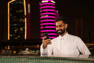 رجل سعودي يستخدم الهاتف الذكي في مدينة ليلية