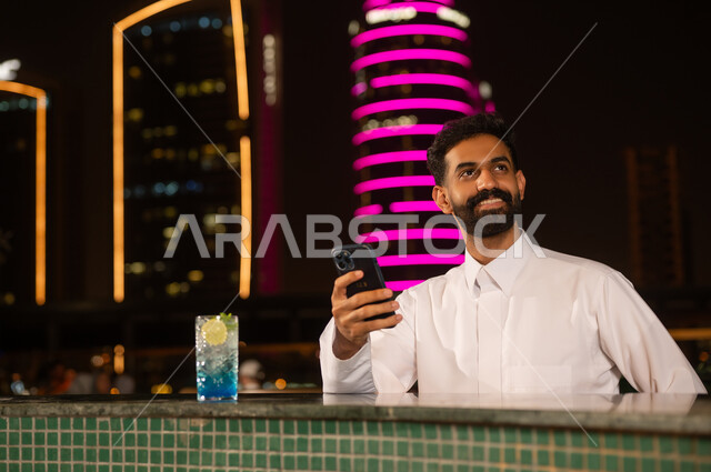 رجل عربي مع هاتف ذكي في جلسة سطح ليلية
