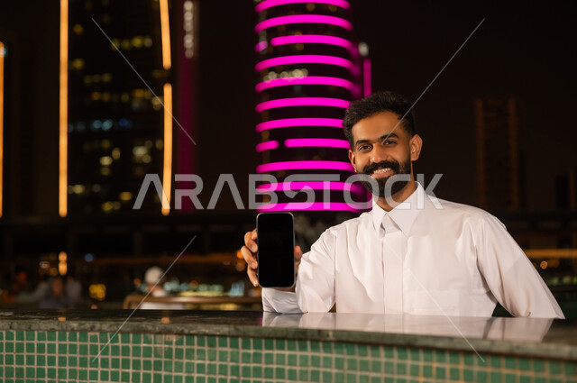 رجل قطري يحمل هاتف ذكي أمام أفق المدينة ليلاً
