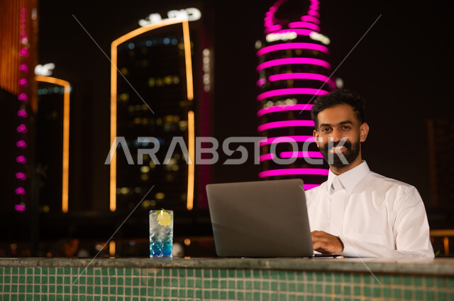رجل عربي يستخدم الكمبيوتر المحمول ليلاً في المدينة
