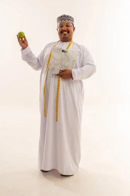 رجل عُماني يحمل ميزان وزن وتفاحة خضراء