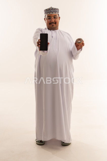 رجل عماني يحمل هاتف ذكي ودونات على خلفية بيضاء
