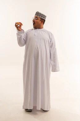 رجل عماني بالزي التقليدي يأكل البيتزا