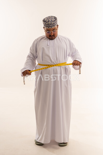 رجل عماني بدين يقيس محيط خصره في الاستوديو