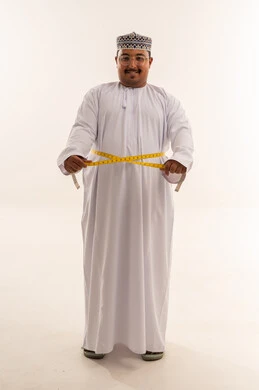 رجل عُماني سمين يقيس محيط خصره بشريط قياس في الاستوديو