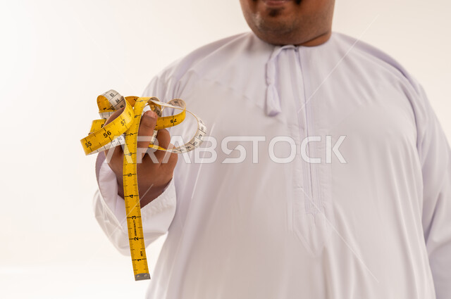 رجل عربي يعاني من السمنة يحمل شريط قياس بالثوب الأبيض
