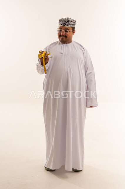 رجل عماني يمسك شريط قياس أمام خلفية بيضاء