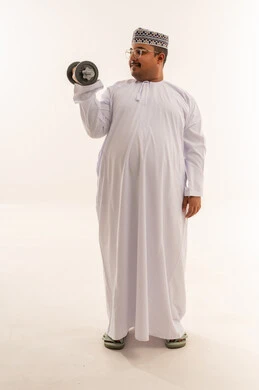 رجل عُماني يمارس الرياضة بالدمبل بالدشداشة التقليدية