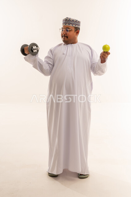 رجل عماني يحمل دمبل وتفاحة في استوديو تصوير