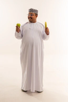 رجل عماني يمسك تفاحة وموزة في الاستوديو