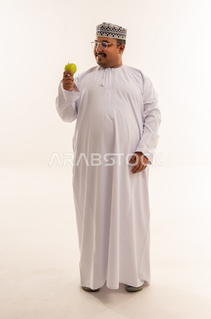 رجل عماني بالزي التقليدي يمسك تفاحة خضراء