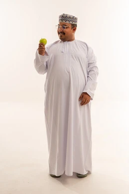 رجل عماني بالزي التقليدي يمسك تفاحة خضراء