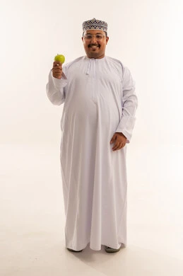 رجل عُماني بالزي التقليدي يمسك تفاحة خضراء
