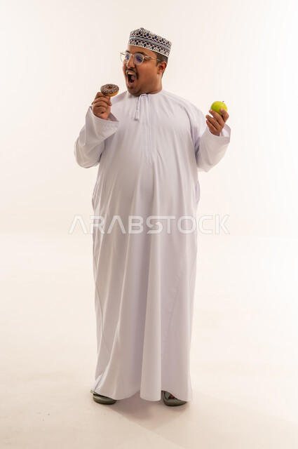 رجل عماني يختار بين الدونات والتفاحة بخلفية بيضاء