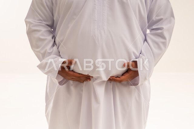 رجل سعودي يعاني من السمنة يمسك بطنه بالثوب الأبيض