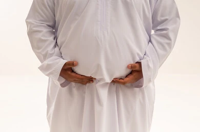 رجل سعودي يعاني من السمنة يمسك بطنه بالثوب الأبيض