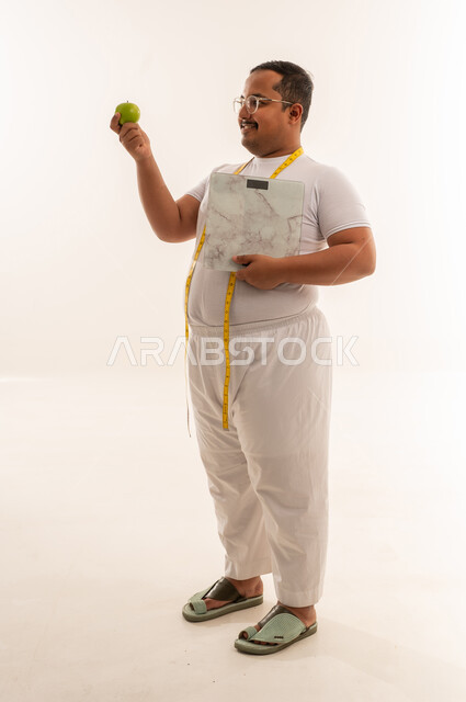 رجل سعودي بوزن زائد مع ميزان وتفاحة خضراء