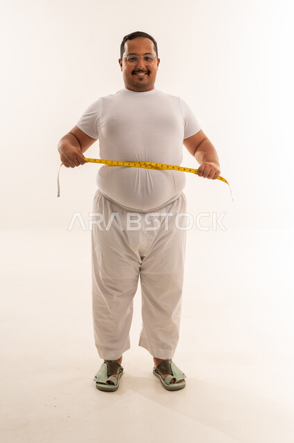 رجل سعودي بدين يقيس خصره في استوديو أبيض