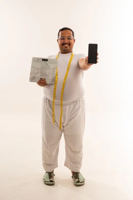 رجل سعودي يعاني من السمنة يحمل ميزان وهاتف