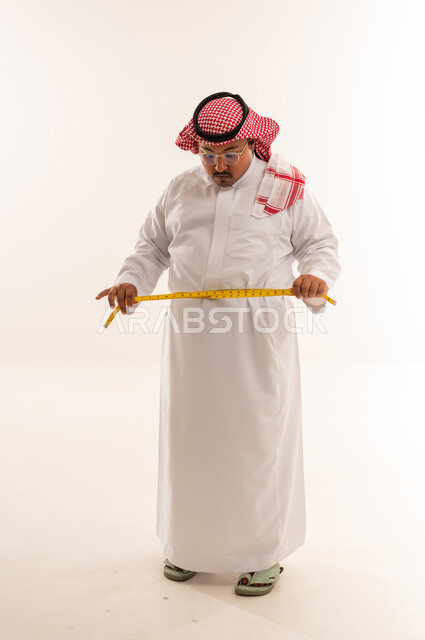 رجل سعودي بدين يقيس خصره في استوديو أبيض