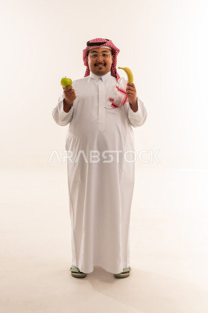 رجل سعودي بدين يمسك بالتفاح والموز في الاستوديو