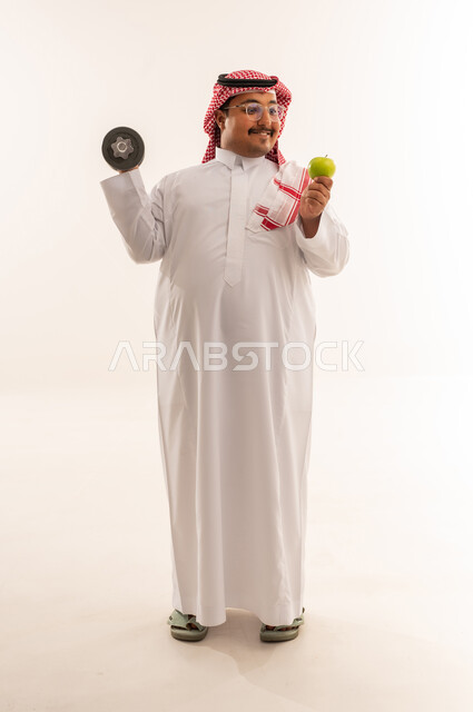 رجل سعودي يحمل دمبل وتفاحة في الاستوديو