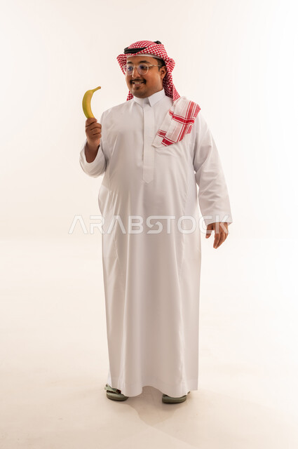 رجل سعودي بدين يمسك موزة في الاستوديو