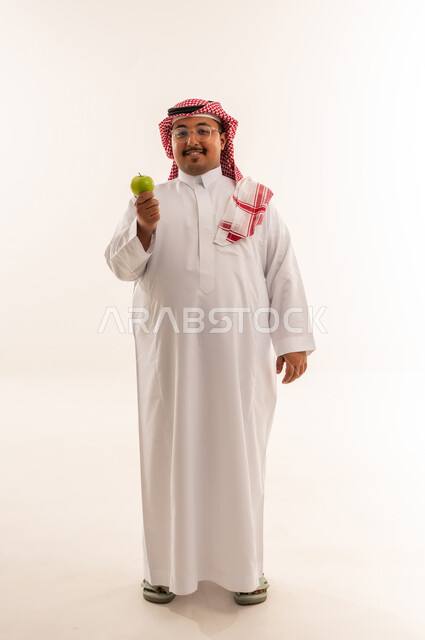 رجل سعودي بالثوب يمسك تفاحة خضراء في الاستوديو