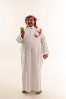 رجل سعودي بالثوب يمسك تفاحة خضراء في الاستوديو