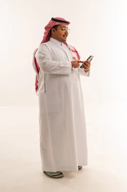 رجل سعودي بالثوب التقليدي يستخدم الهاتف الذكي