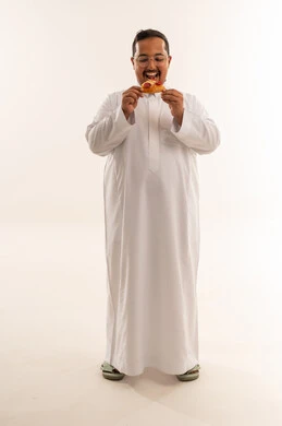 رجل سعودي بدين يبتسم ويأكل بيتزا ببروني بالثوب الأبيض
